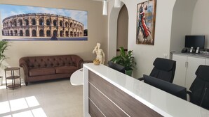 A reception area with a sofa, a statue, a painting, a TV, and a desk. - Square Hôtel (Nîmes)