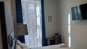Un dormitorio con cama, escritorio, silla, televisión y ventana con cortinas.