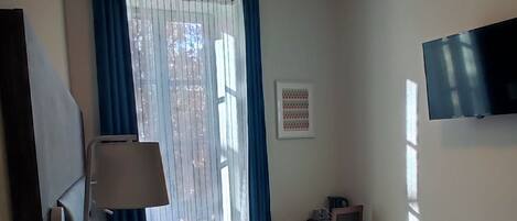 Un dormitorio con cama, escritorio, silla, televisión y ventana con cortinas.