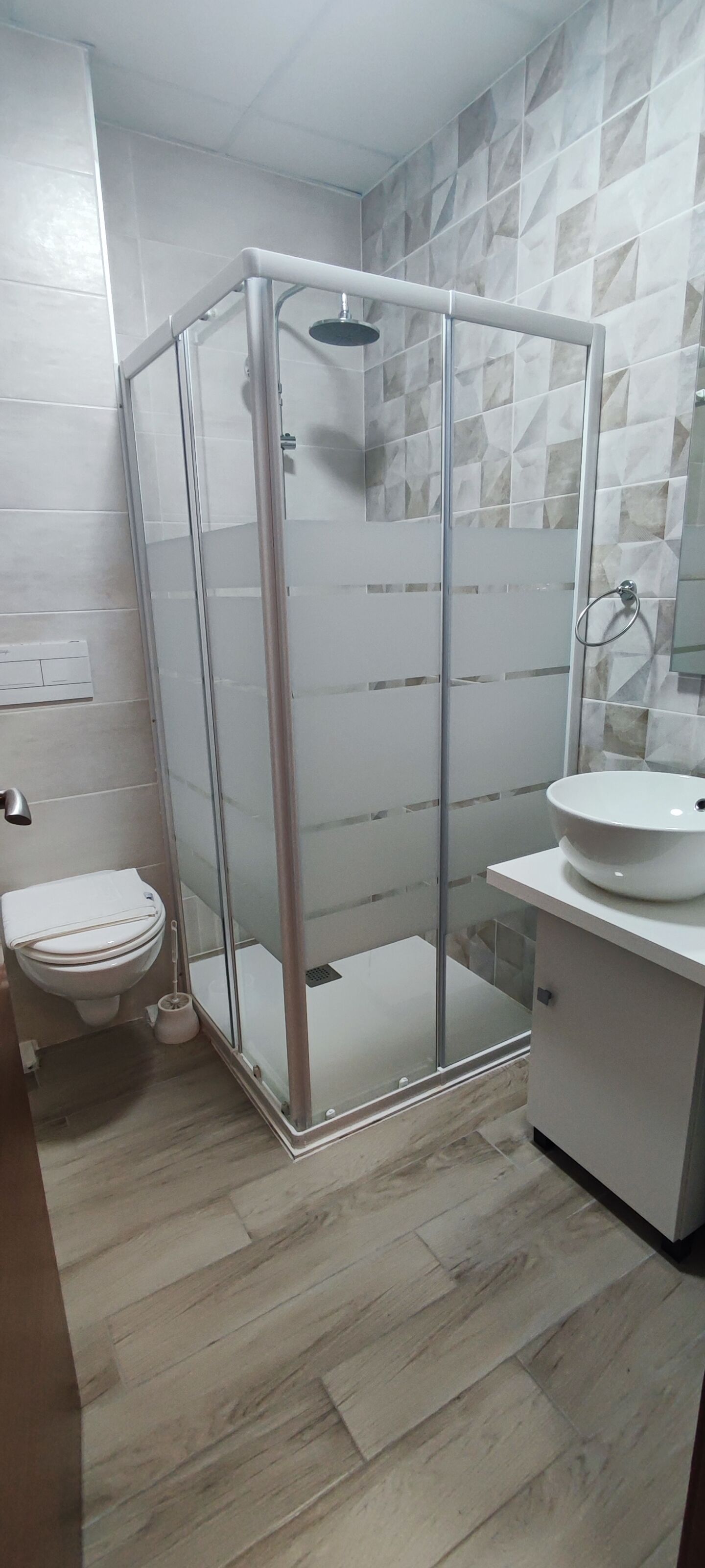 A bathroom with a glass-enclosed shower, a white toilet, and a sink on a white countertop.