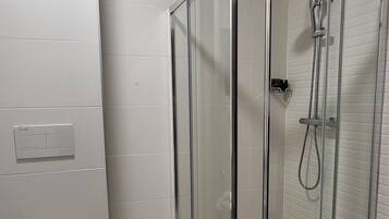 Un baño moderno con ducha separada por mampara de vidrio, inodoro y un aplique de pared.