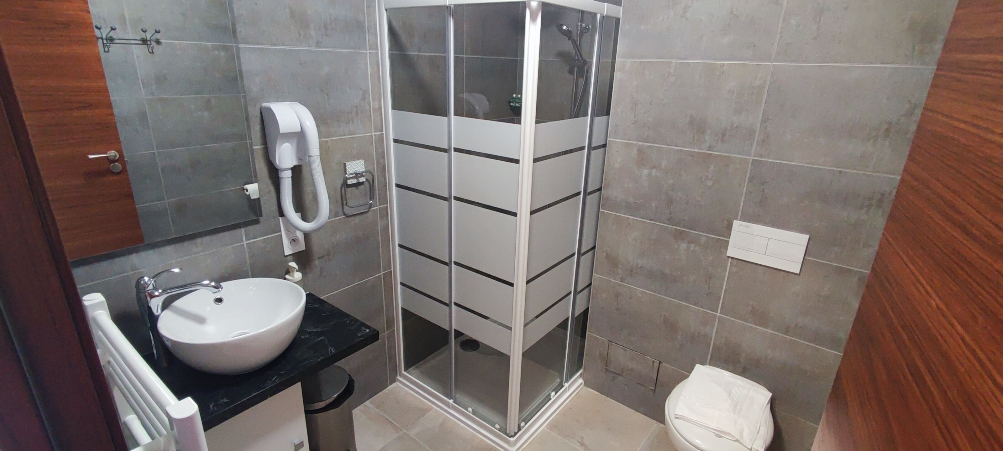 A bathroom with a sink, mirror, towel rack, shower, and toilet.