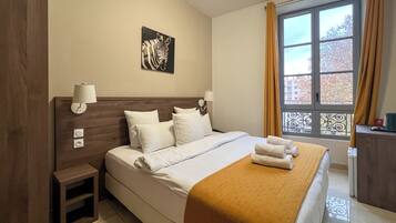 Habitación de hotel con una cama grande, una mesita de noche, una lámpara de pared, una ventana con cortinas y una obra de arte con estampados de cebra en la pared.