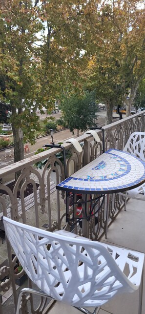 A balcony with a tiled table and white plastic chairs, surrounded by ornate metal railings.