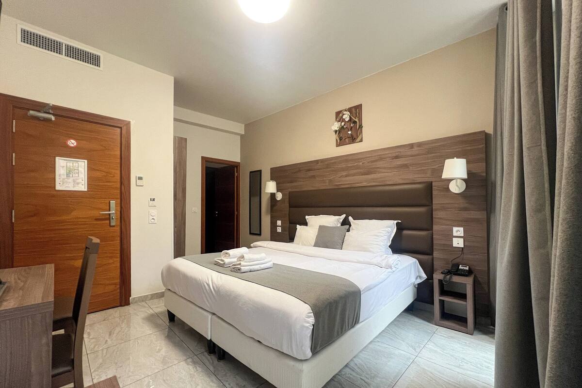 A hotel room with a large bed, a bedside table, a lamp, and a door with a no-smoking sign.
