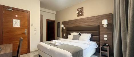 A hotel room with a large bed, a bedside table, a lamp, and a door with a no-smoking sign.