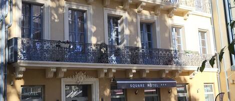 A multi-story building with balconies, a sign reading "SQUARE HOTEL," and potted plants in the foreground.