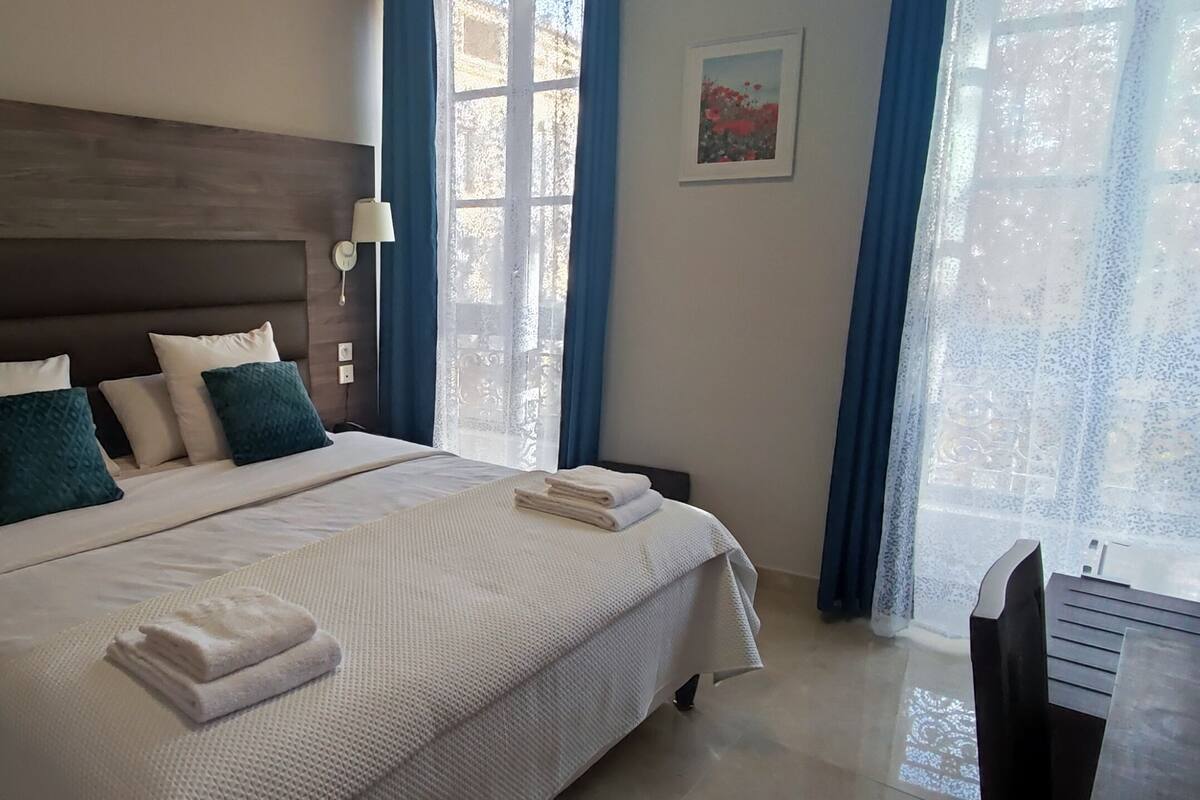A hotel room with a large bed, two bedside lamps, a window with curtains, and a framed picture on the wall.
