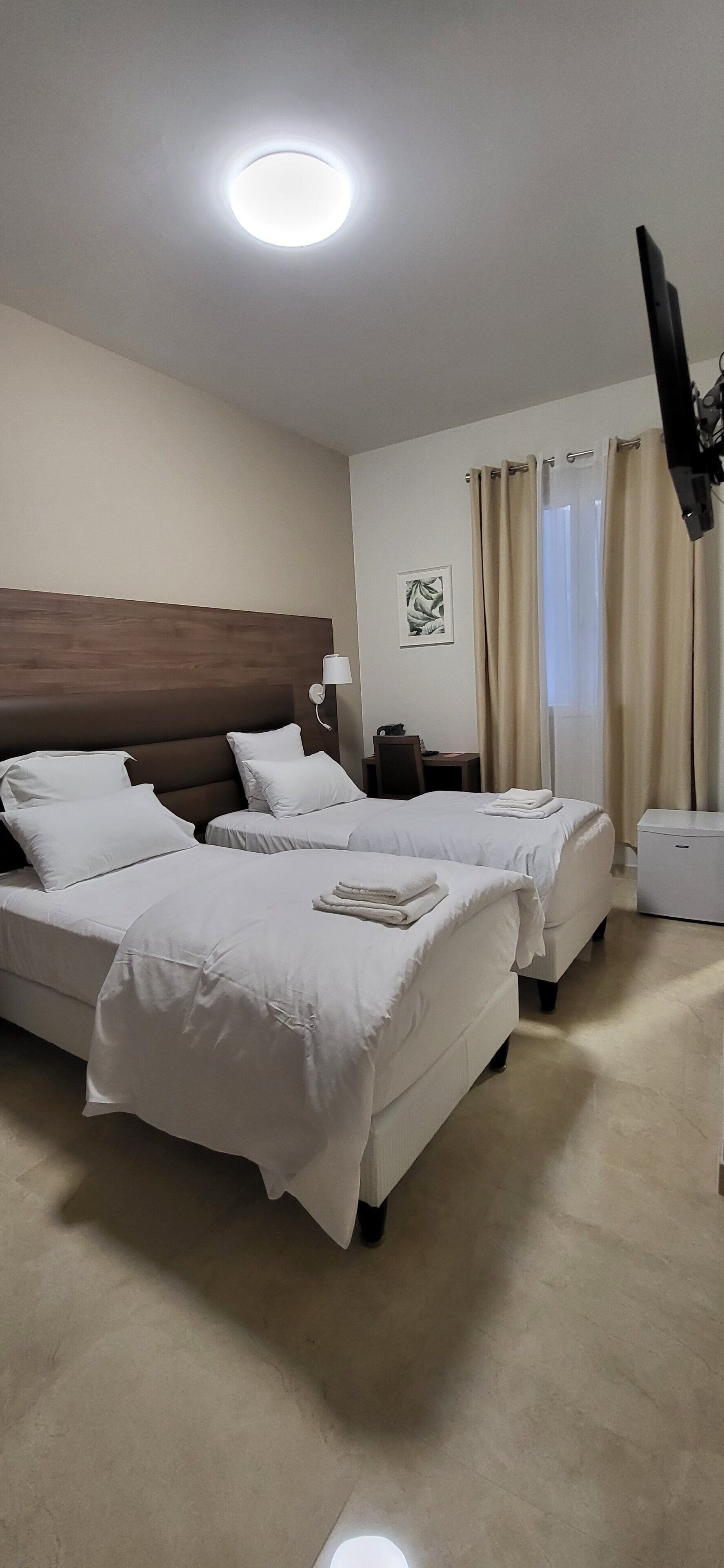 A hotel room with two beds, a desk, a chair, a TV, and a window with curtains.