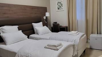 A hotel room with two beds, a desk, a chair, a TV, and a window with curtains.