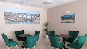 A conference room with green chairs and a table, two large wall murals, and a potted plant. - Square Hôtel (Nîmes)
