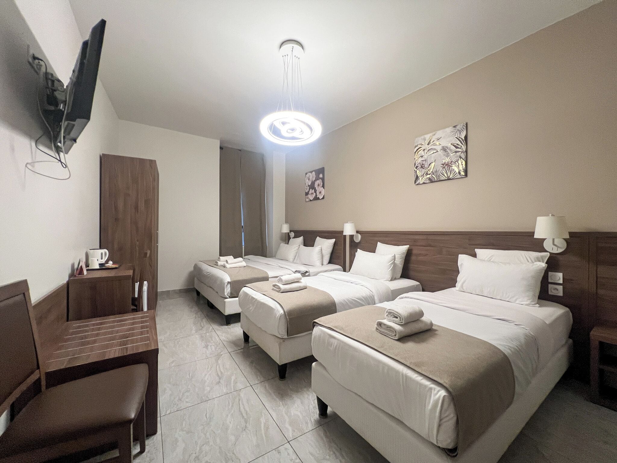 Habitación de hotel con dos camas, un escritorio, una silla, un televisor montado en la pared y una lámpara en el techo.
