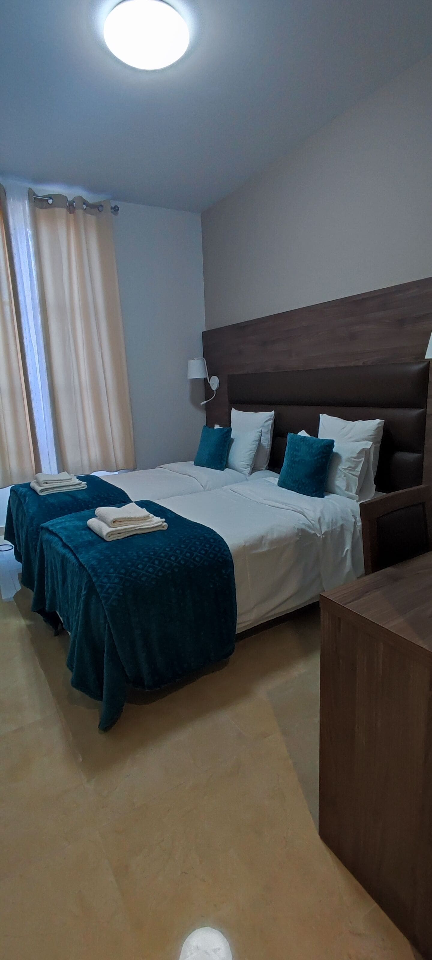 Una camera d'albergo con due letti, una testiera in legno, una scrivania e una finestra con tende.