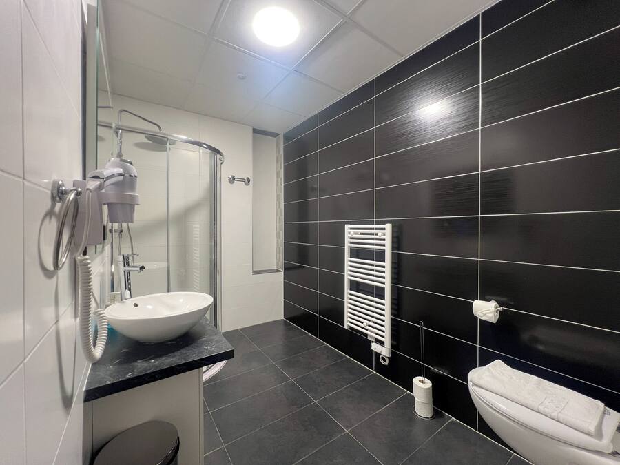 Une salle de bain moderne avec une douche à l’italienne en verre, un lavabo blanc et un mur recouvert de carreaux noirs.