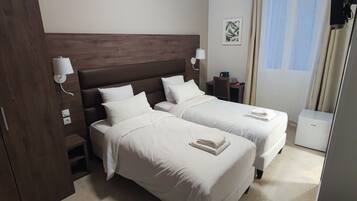 A hotel room with two beds, a wooden headboard, bedside lamps, a small table, and a window with curtains.