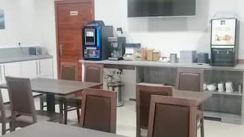 Un área de cocina moderna con una cafetera, un dispensador de fruta y un televisor montado en la pared.