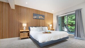 Camera da letto moderna con un letto grande, parete rivestita in legno e vista sul verde attraverso una porta scorrevole in vetro.