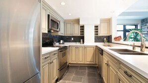 Een moderne keuken met roestvrijstalen apparatuur, lichte houten kastjes en een zwart betegelde spatwand.