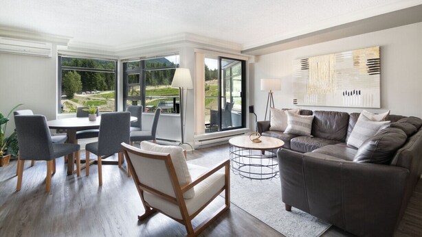 Een moderne woonkamer met een groot raam, een bank, een salontafel en een eethoek met stoelen.
