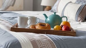 Een netjes opgemaakt bed met een dienblad vol ontbijtartikelen, zoals gebak, fruit en een theepot.