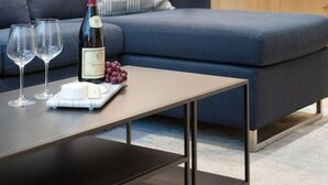 A modern living room with a sofa, a coffee table, and a bottle of wine. - MAGNIFICENT SKI-IN/OUT 1BR: AC and Gym (Whistler)