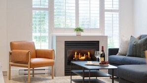 A living room with a fireplace, a sofa, a chair, and a table with snacks and drinks. - MAGNIFICENT SKI-IN/OUT 1BR: AC and Gym (Whistler)
