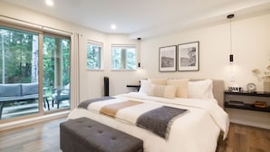 Une chambre moderne avec un grand lit, un banc et une vue sur une terrasse accessible par des portes vitrées.