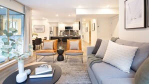 Un salon moderne avec un canapé, deux fauteuils, une table basse et, au fond, un coin repas.