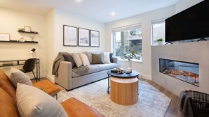 Un salon moderne avec un canapé gris, une table basse ronde en bois, une cheminée et un téléviseur fixé au mur.