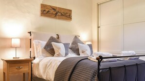 Un lit bien fait, recouvert d’une couverture matelassée, une table de chevet avec une lampe et une œuvre d’art représentant des oiseaux accrochée au mur.