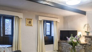 Un salon avec une cheminée en pierre, un téléviseur, un canapé et deux petites tables sur lesquelles est posé un vase de fleurs.