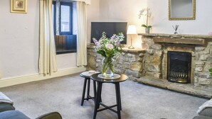 Un salon chaleureux avec une cheminée en pierre, un téléviseur et un vase rempli de fleurs posé sur une petite table.
