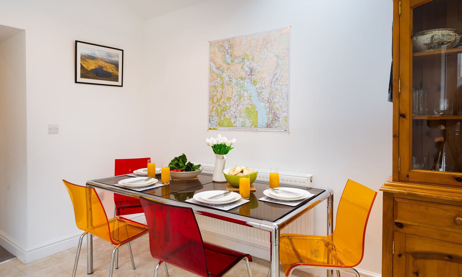 A dining area with a table set for four, red chairs, a map on the wall, and a cabinet with glass doors.