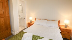 A neatly made bed with a green quilt, two bedside lamps, and a wooden wardrobe in a hotel room. - Millerbeck (Ambleside)