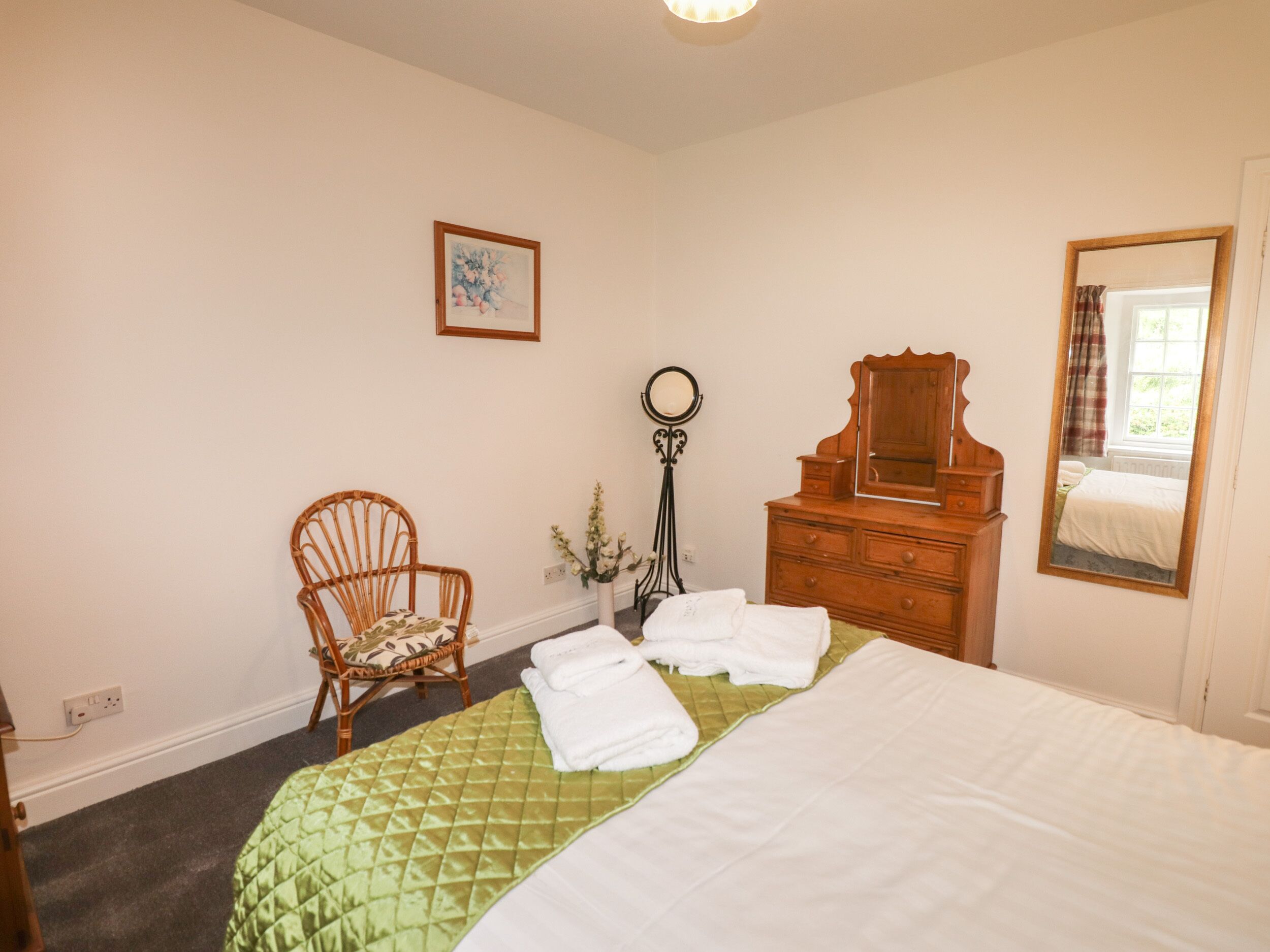 Un dormitorio con cama, cómoda de madera, silla, espejo y un cuadro en la pared.