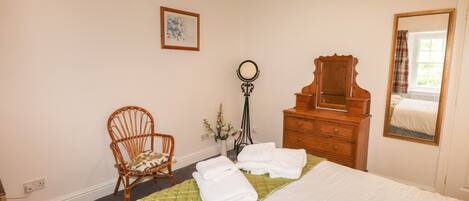 Un dormitorio con cama, cómoda de madera, silla, espejo y un cuadro en la pared.