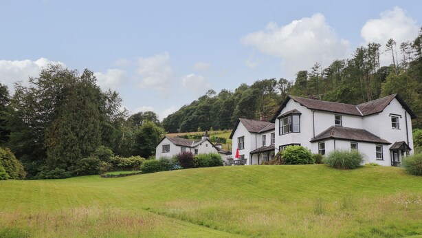 A row of white houses with pitched roofs, surrounded by lush greenery and a clear sky. - Millerbeck (Ambleside)