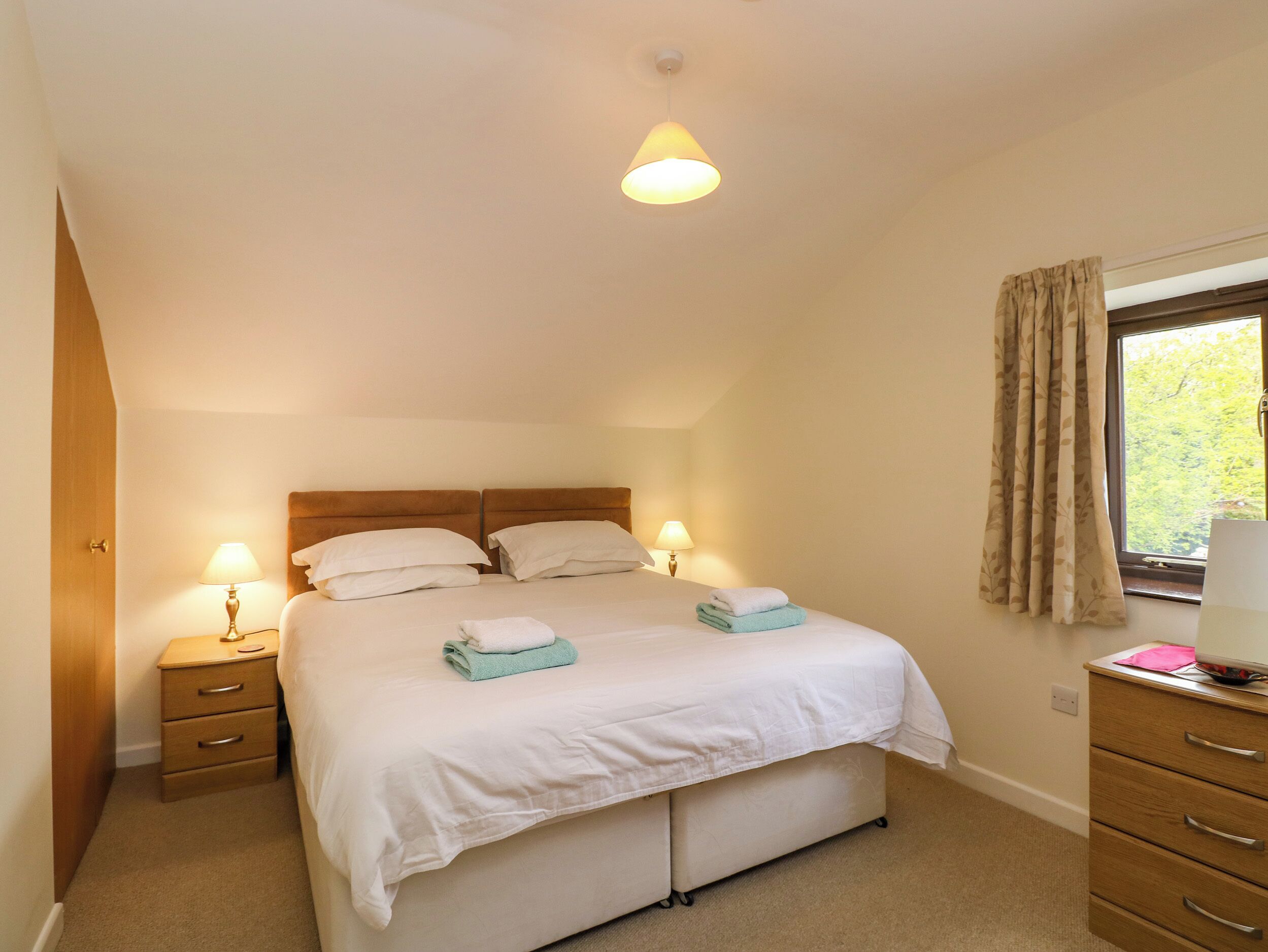 Une chambre avec un lit simple, deux tables de chevet, une fenêtre avec des rideaux et un luminaire au plafond.