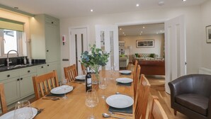 Comedor con una mesa de madera dispuesta para seis personas, rodeada de sillas. Un jarrón con follaje verde está sobre la mesa.