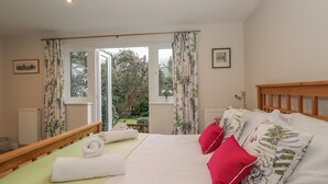Un dormitorio con cama, almohadas y vistas a un jardín a través de un ventanal grande.