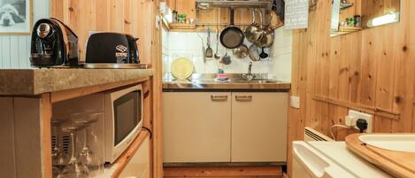 A compact kitchen with wooden walls, a microwave, a sink, and various utensils hanging above.