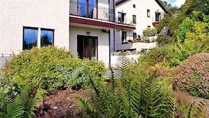 A multi-story building with balconies and a garden with various plants.