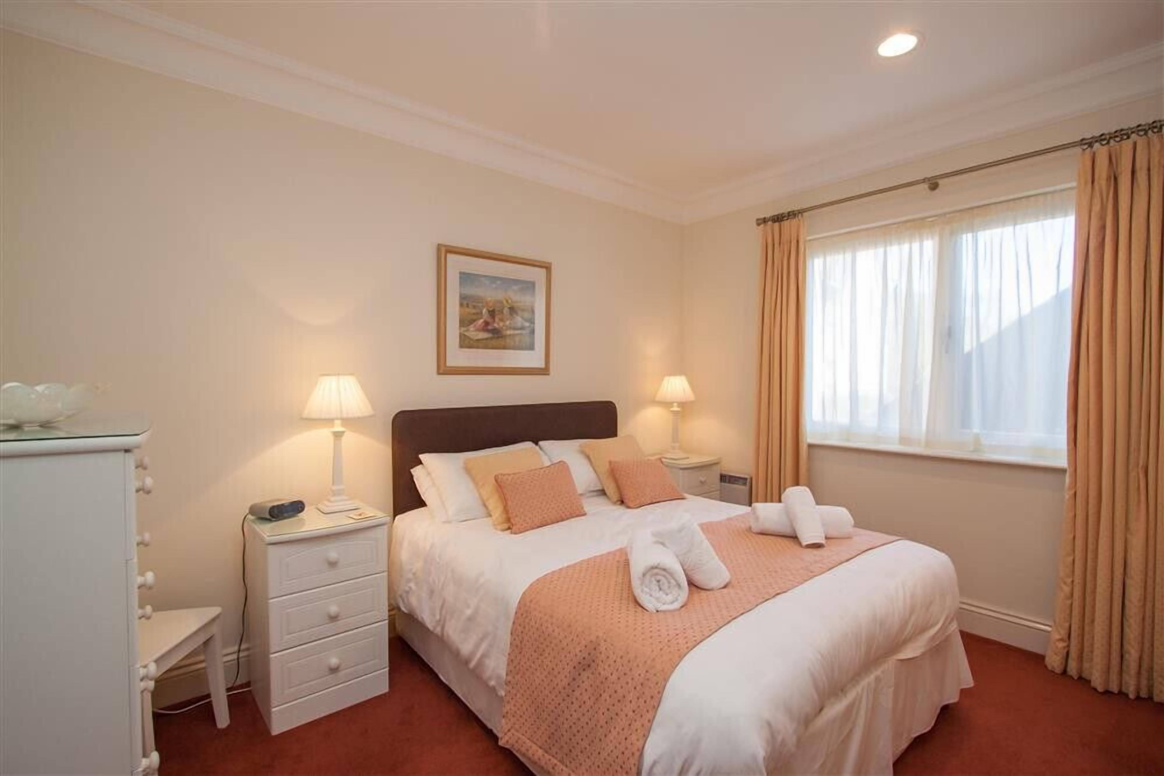 A neatly arranged hotel room with a bed, two bedside tables, a nightstand, a dresser, and a window with curtains.