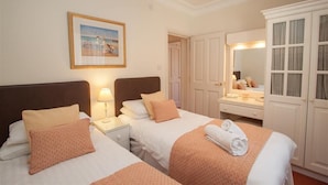 A hotel room with two beds, a bedside table with a lamp, a dresser with a mirror, and a framed picture on the wall.