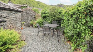 Un bâtiment en pierre avec un toit en pente, une terrasse en gravier et une table ronde entourée de chaises.