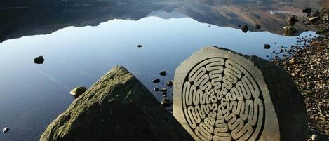 A clear lake with a large rock featuring a circular pattern.