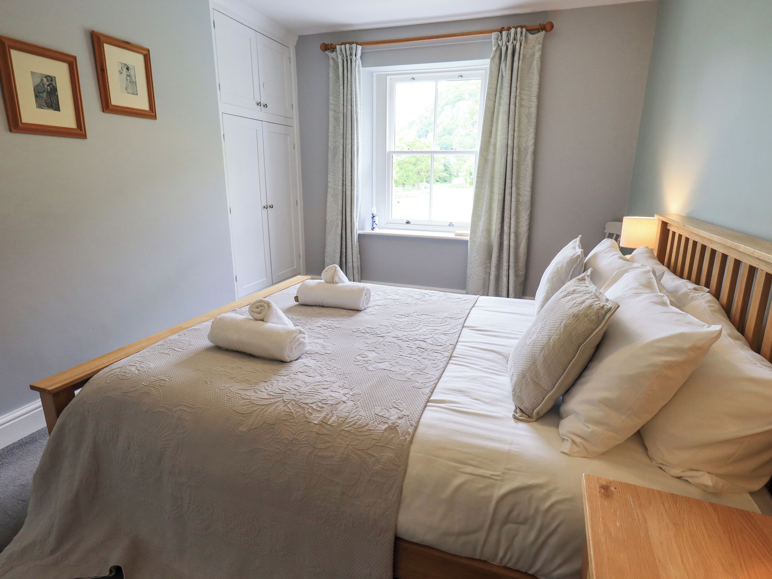 Ein Schlafzimmer mit einem großen Bett, zwei zusammenge rollten Handtüchern, einem Fenster mit Vorhängen und einem Kleiderschrank.