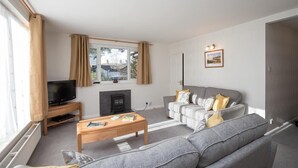 A living room with a grey sofa, a wooden coffee table, a television on a stand, and a fireplace. - Yew Tree Cottage (Ambleside)