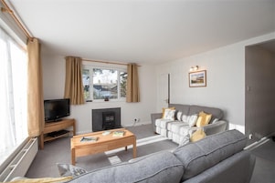A living room with a grey sofa, a wooden coffee table, a television on a stand, and a fireplace.