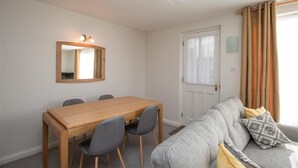 A room with a wooden dining table, grey sofa, and a mirror on the wall. - Yew Tree Cottage (Ambleside)